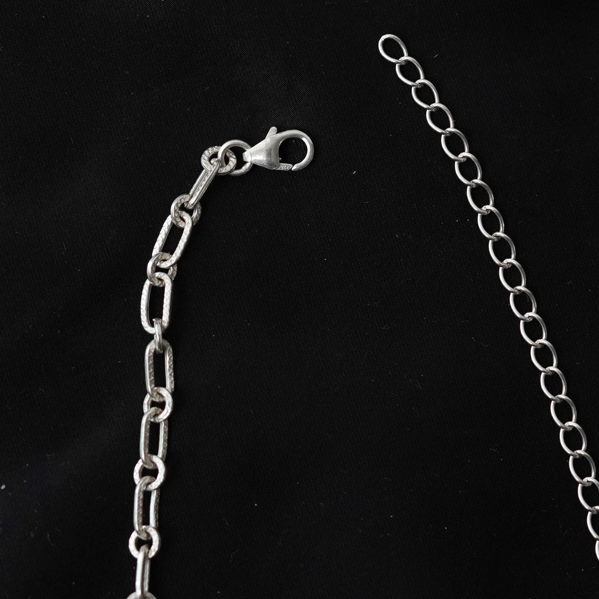 A close-up view of a 925 silver chain extender with a lobster clasp on a black background.