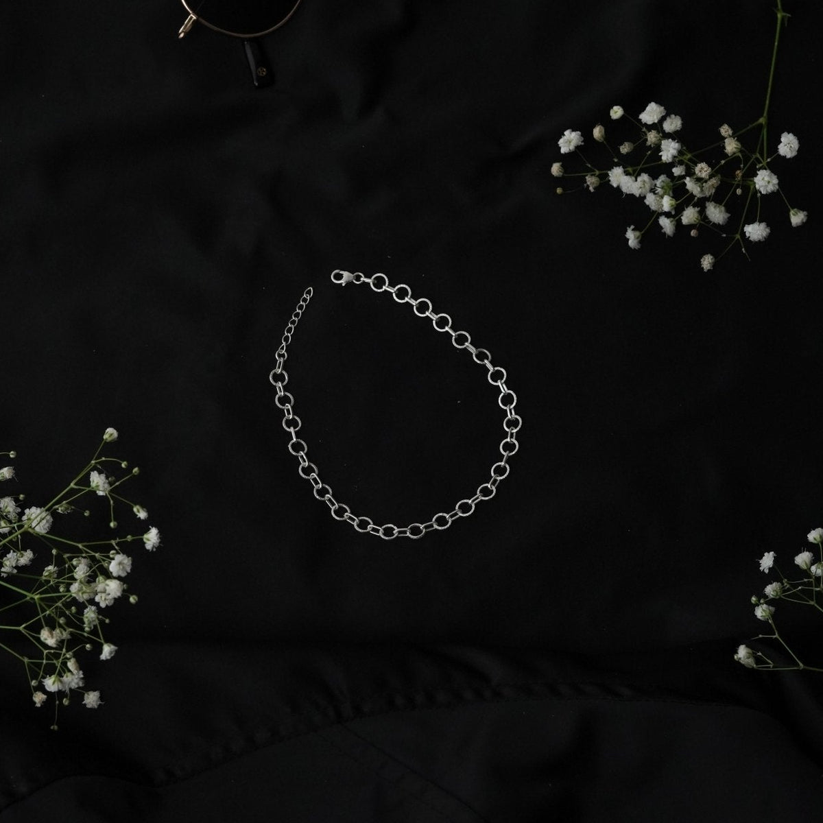 925 Silver chain bracelet on a dark black fabric background with small white flowers.
