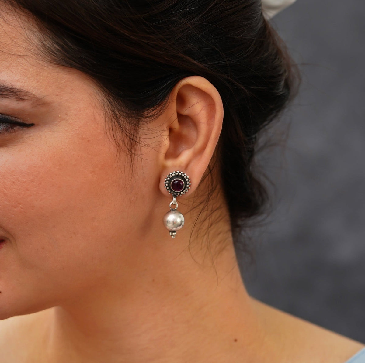 side view of a woman wearing a 925 sterling silver earring with a red stone  oxidized finish hanging with a silver round ball.