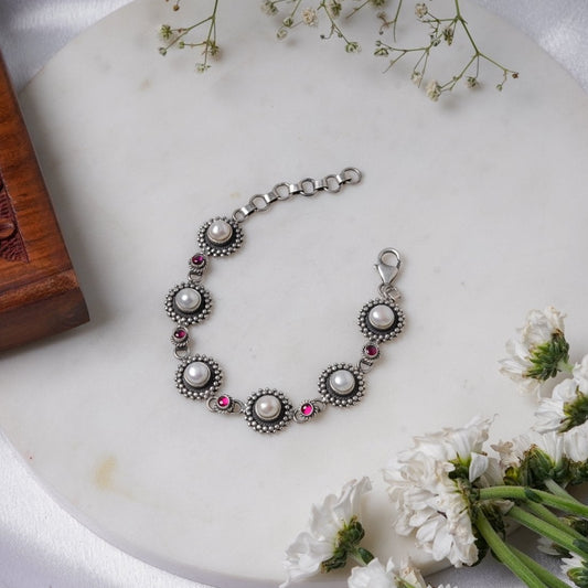 sterling silver link bracelet with pearls and red stones on a white surface with flowers.