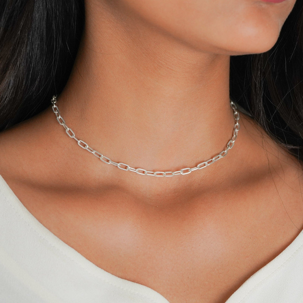 A close-up of a model wearing a delicate 925 silver paperclip chain necklace, styled with a white top.