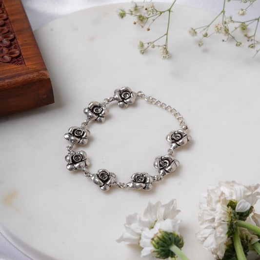 Oxidized 925 Silver link bracelet with rose-shaped charms on a white surface with flowers