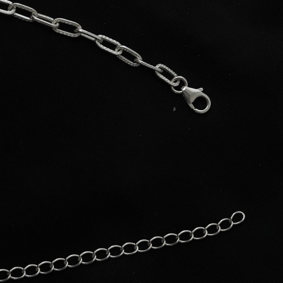 A close-up of a 925 silver chain anklet with elongated oval links and a lobster clasp, shown on a black background with a second section of chain at the bottom.