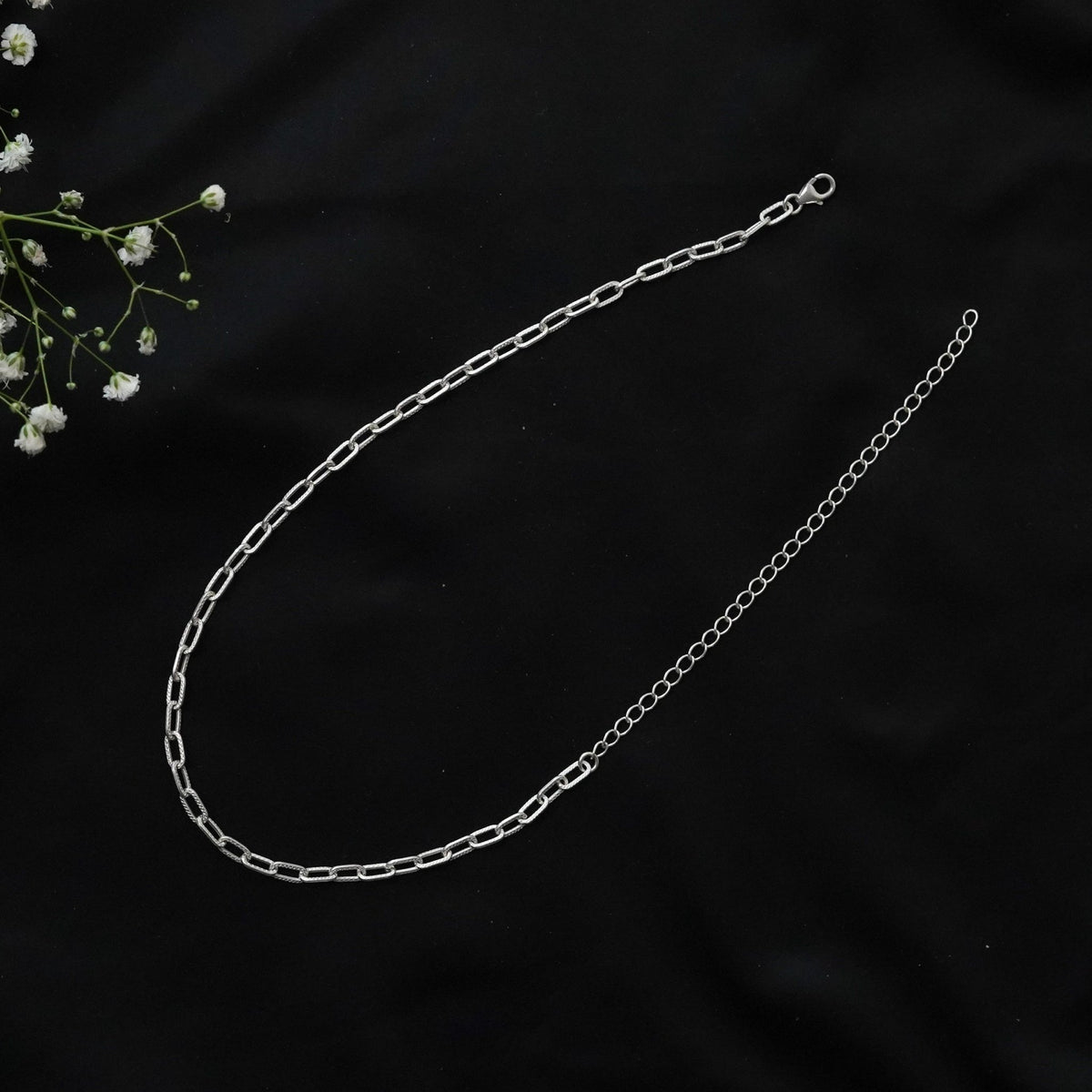 Featuring a 925 silver paperclip chain necklace with a lobster clasp, displayed on a black fabric background with white flowers.
