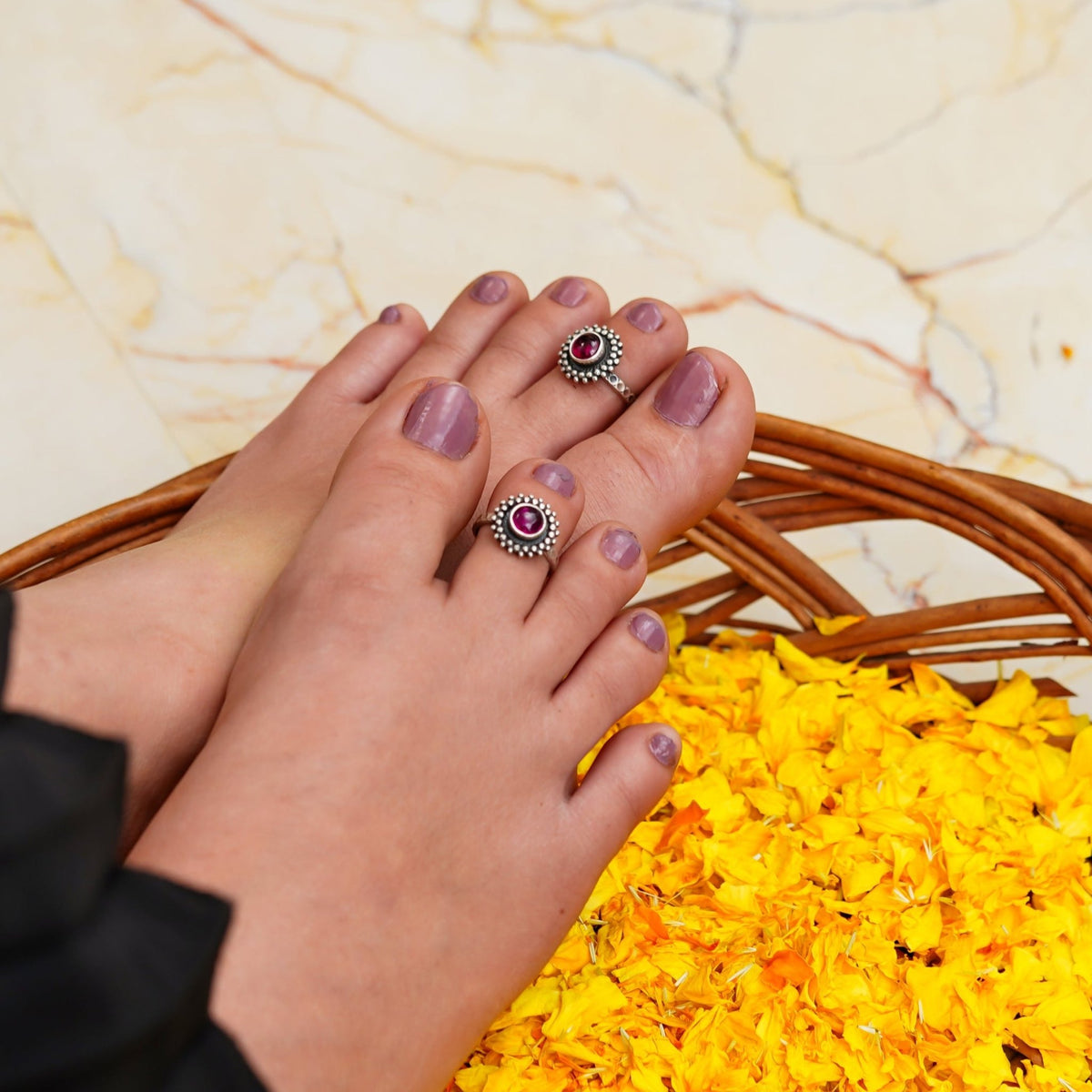 Close-up of feet wearing silver toe rings/bichiya with red stones on a yellow flower bed.