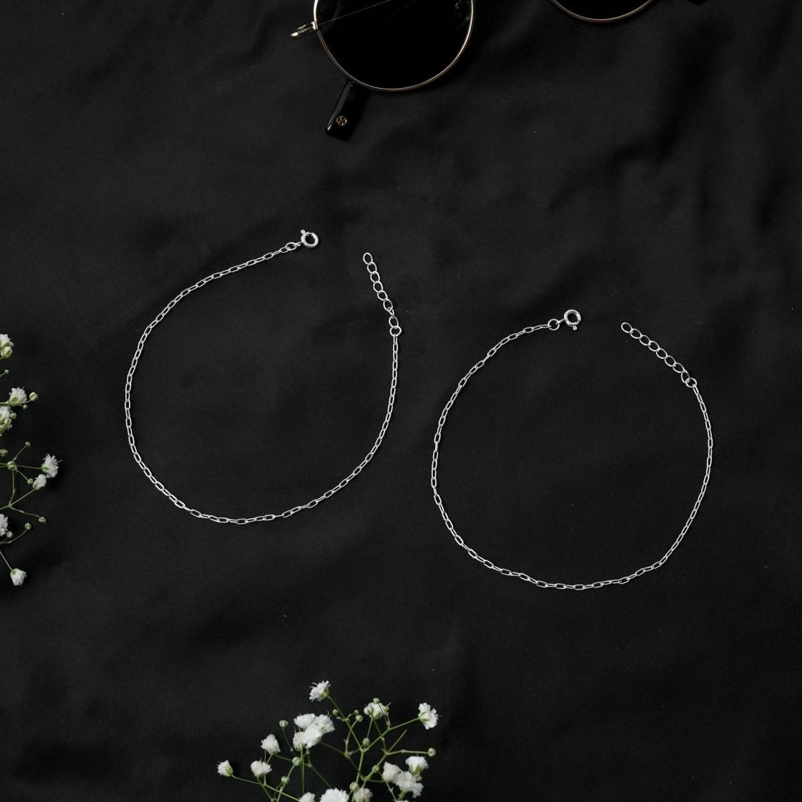 dailywear a pair of 925 silver anklet payal for women on a dark surface with small white flowers.